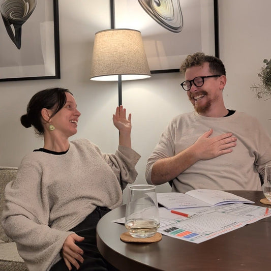 A man and a woman sit playing the date night game, both are laughing